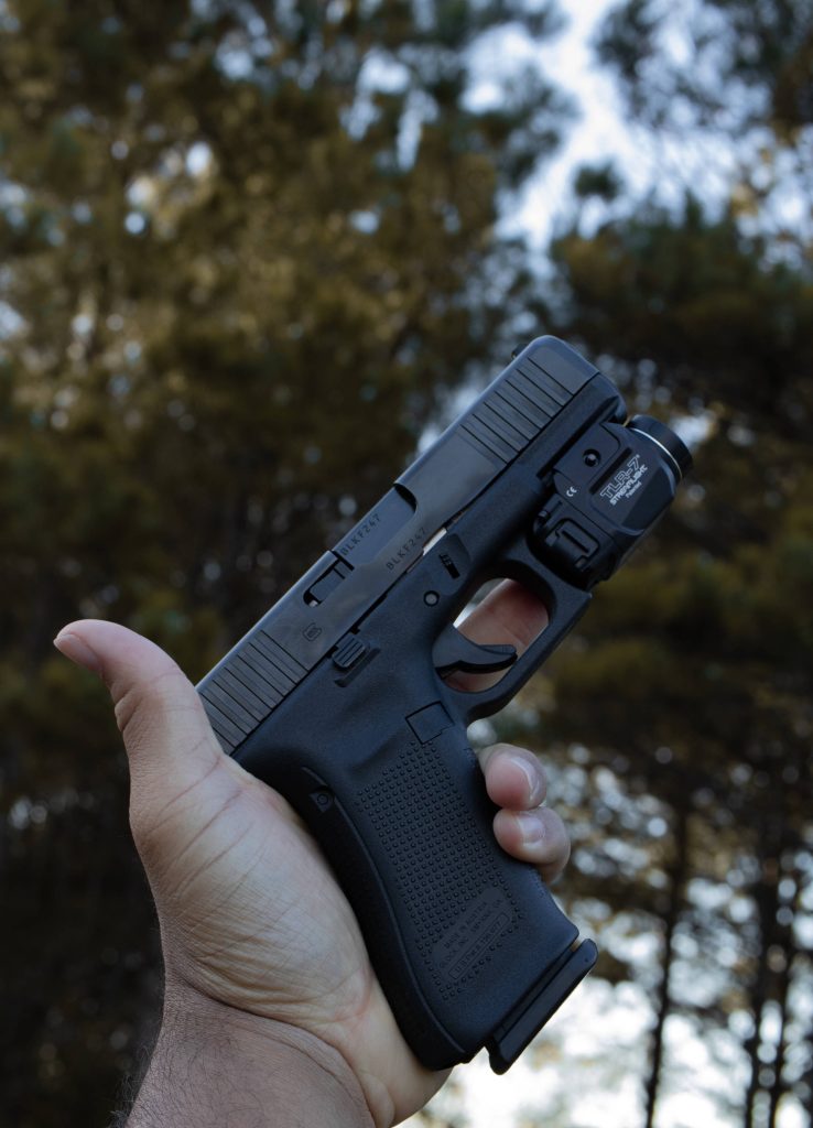 Hand gripping black Glock pistol with Streamlight TLR-7 light in daylight forest background wallpaper