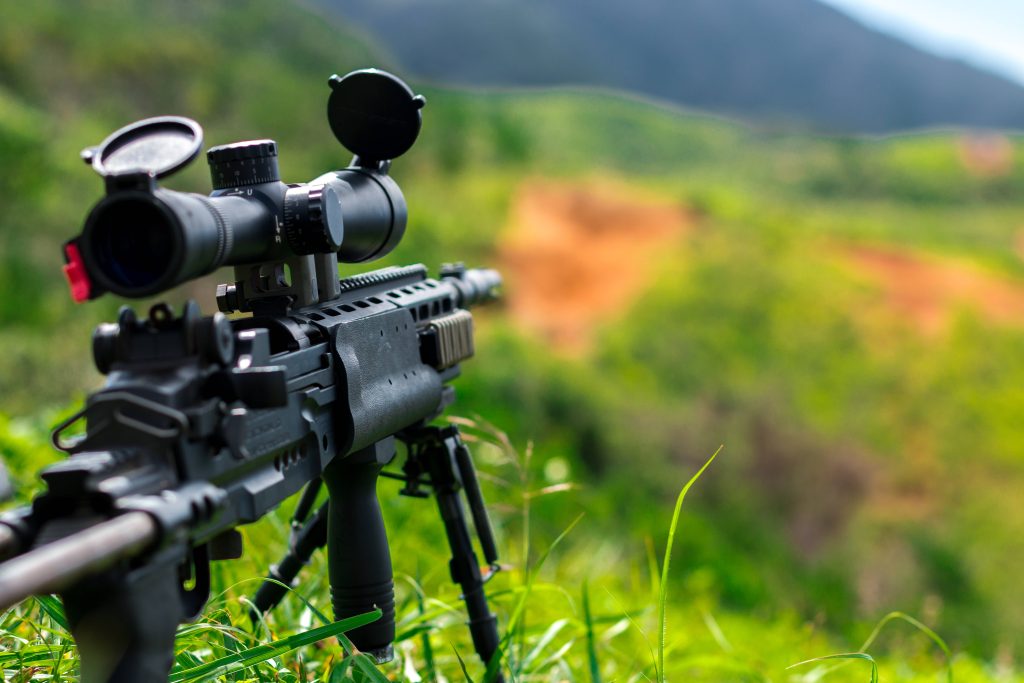 Tactical M14 EBR rifle on bipod in grass with scoped optic and blurred mountain background wallpaper