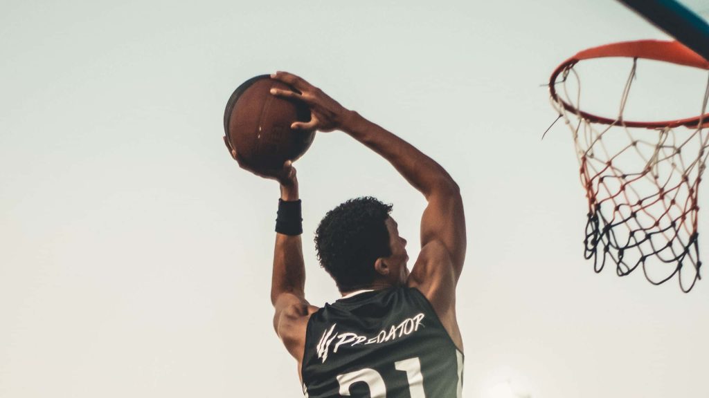 Athletic basketball player in black Predator jersey number 21 jumping for a shot outdoors Wallpaper