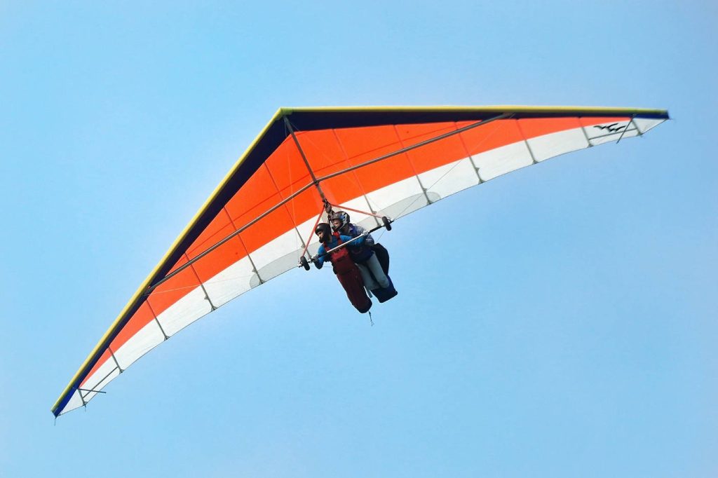Couple hang gliding tandem above clouds vibrant blue sky adventurous air sports wallpaper