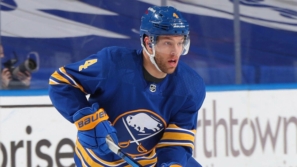 Taylor Hall Buffalo Sabres blue jersey mid-action ice hockey intense focus dynamic arena background Wallpaper