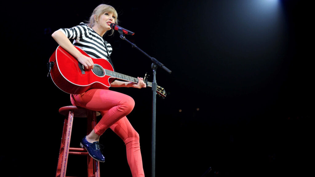 Taylor Swift acoustic Red performance on stage with red guitar under bright concert lights Wallpaper