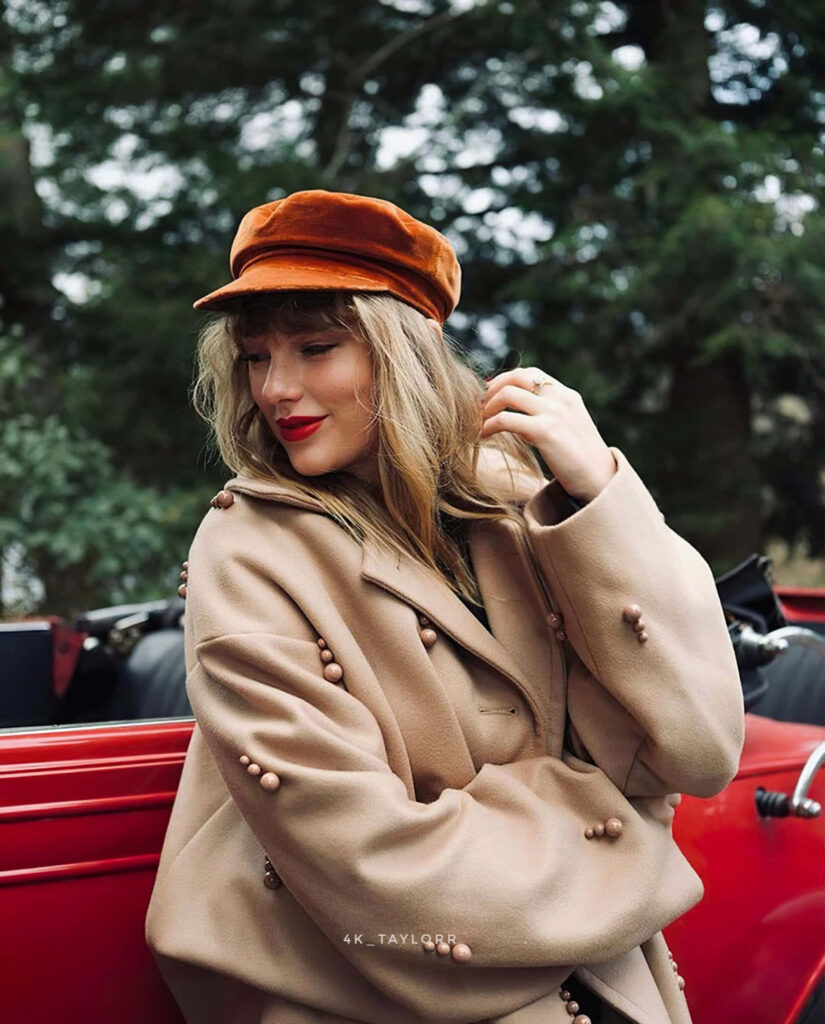 Taylor Swift in tan coat and red cap by classic red convertible inspired by Red Taylor's Version Wallpaper