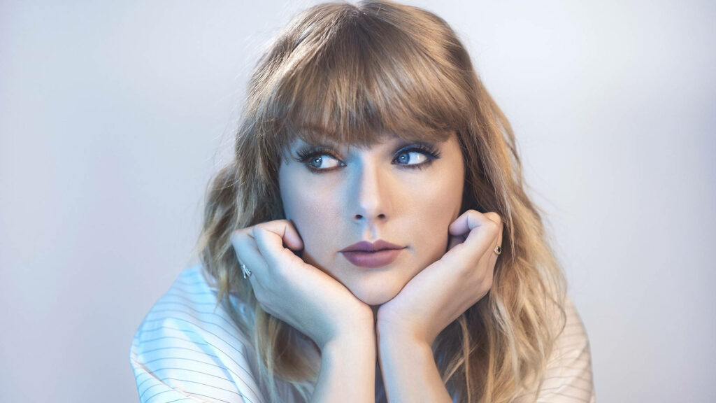 Taylor Swift in a reflective thoughtful pose resting chin on hands against soft light background Wallpaper