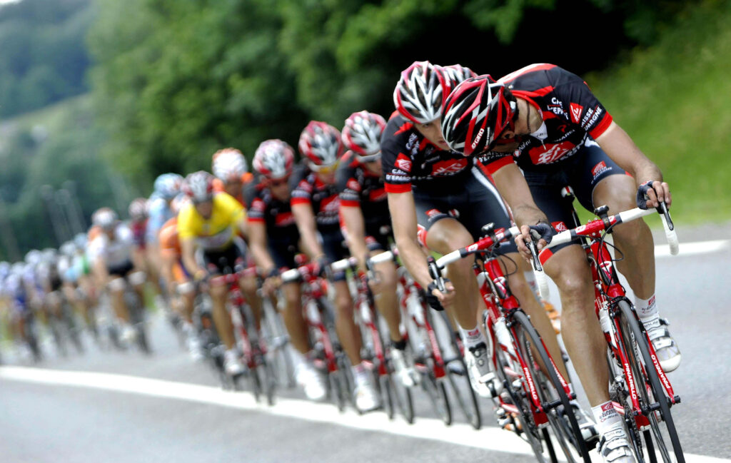 Cyclists in matching gear race on scenic road showcasing teamwork intensity and vibrant motion Wallpaper
