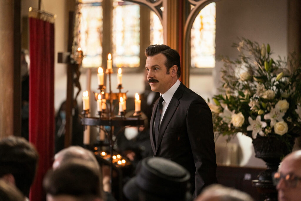 Heartfelt Ted Lasso Funeral Scene Wallpaper with Candles & Flowers