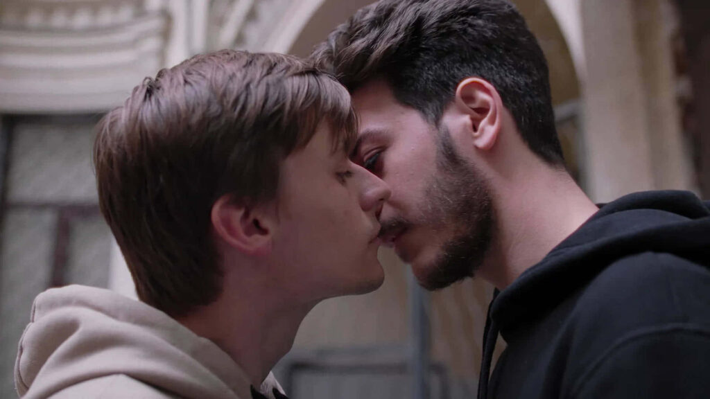 Two young men sharing a gentle kiss showing love and connection in an urban wallpaper background