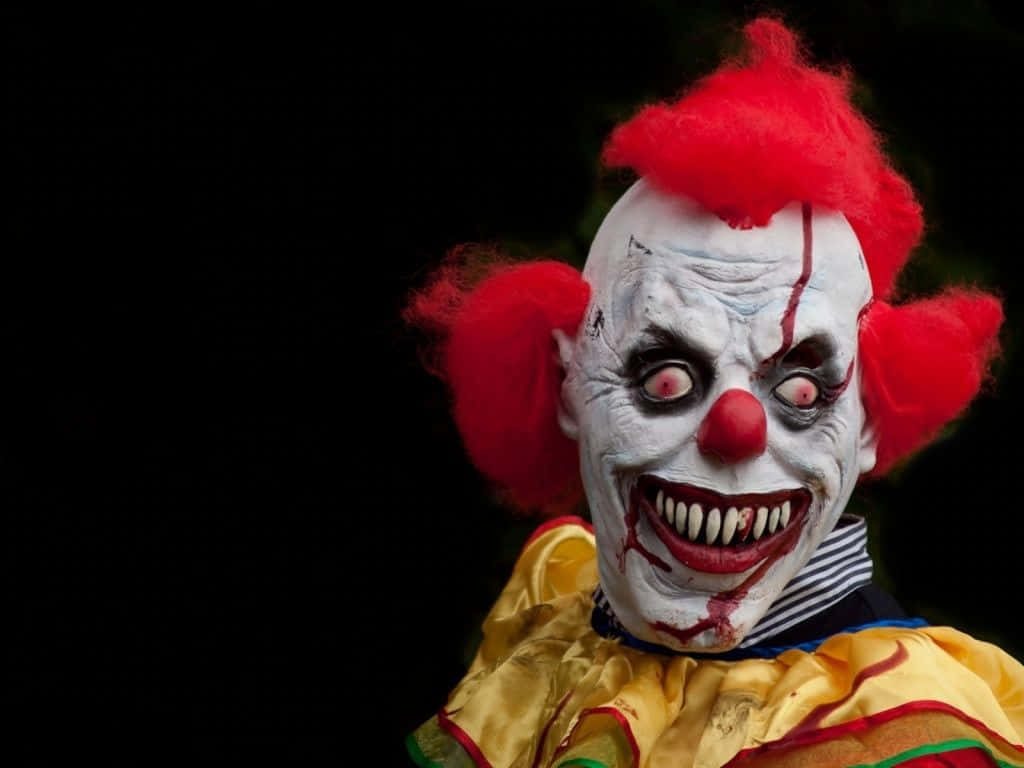Terrifying horror clown with pale face sharp teeth red hair yellow collar on black background wallpaper