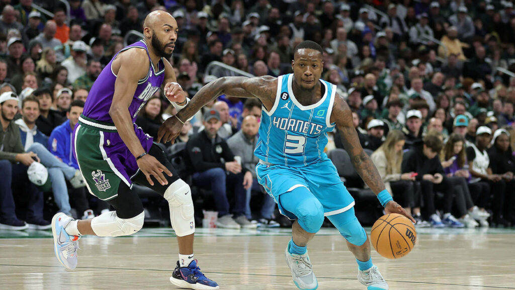 Terry Rozier in teal Charlotte Hornets jersey drives past Milwaukee Bucks defender in packed NBA arena Wallpaper