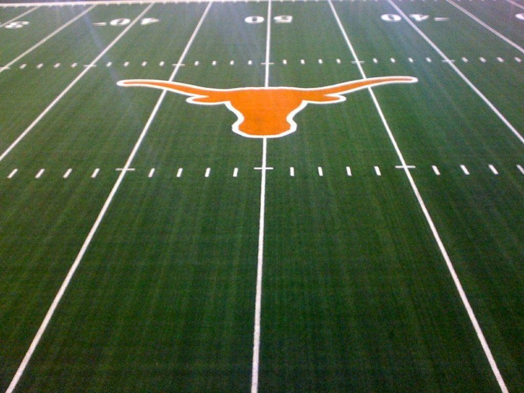 Texas Longhorns football field with iconic burnt orange steer logo at 50-yard line green turf Wallpaper
