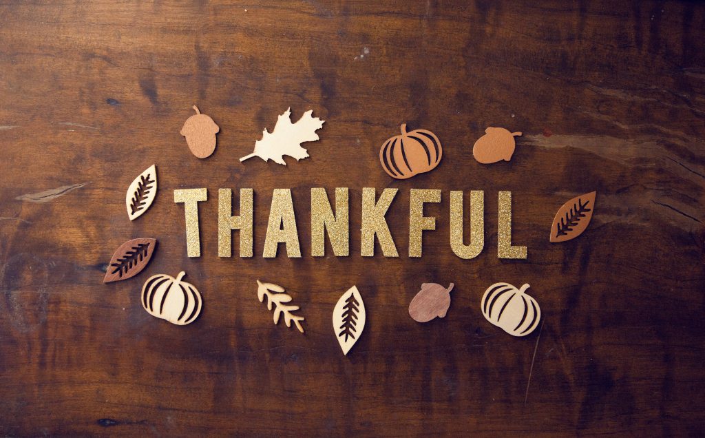 Thankful in gold glitter surrounded by autumn leaves pumpkins and acorns on wood background Wallpaper