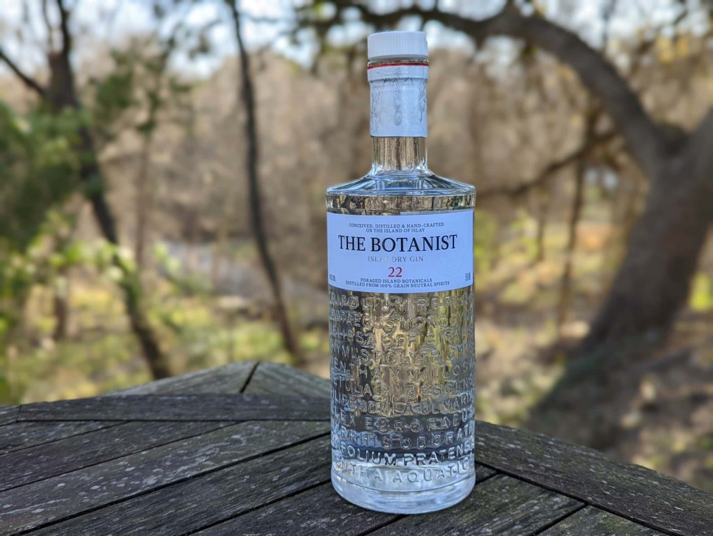 The Botanist Islay Dry Gin bottle on weathered wood with forest background premium gin wallpaper