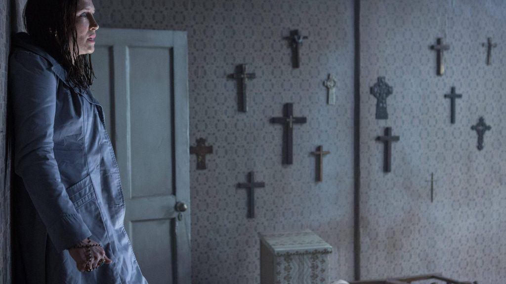 Lorraine Warren in dimly lit crucifix room wallpaper from The Conjuring horror movie scene