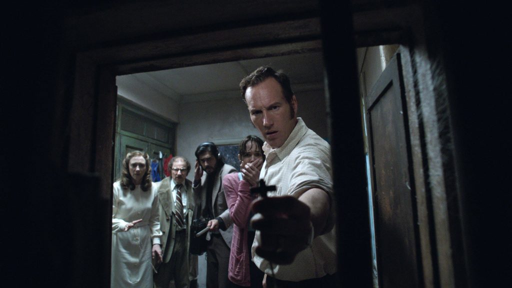 Ed Warren holding cross in dark tense exorcism scene from The Conjuring horror movie wallpaper