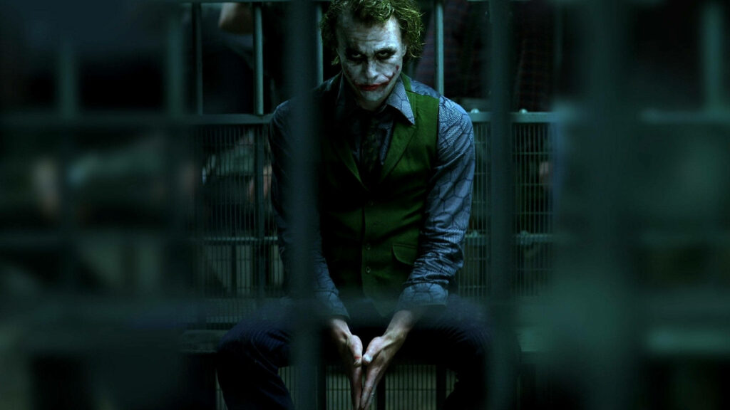 The Joker's Haunting Incarceration: A Captivating Still from 'The Dark Knight' featuring Heath Ledger as the Iconic Clown Prince behind Prison Bars Wallpaper