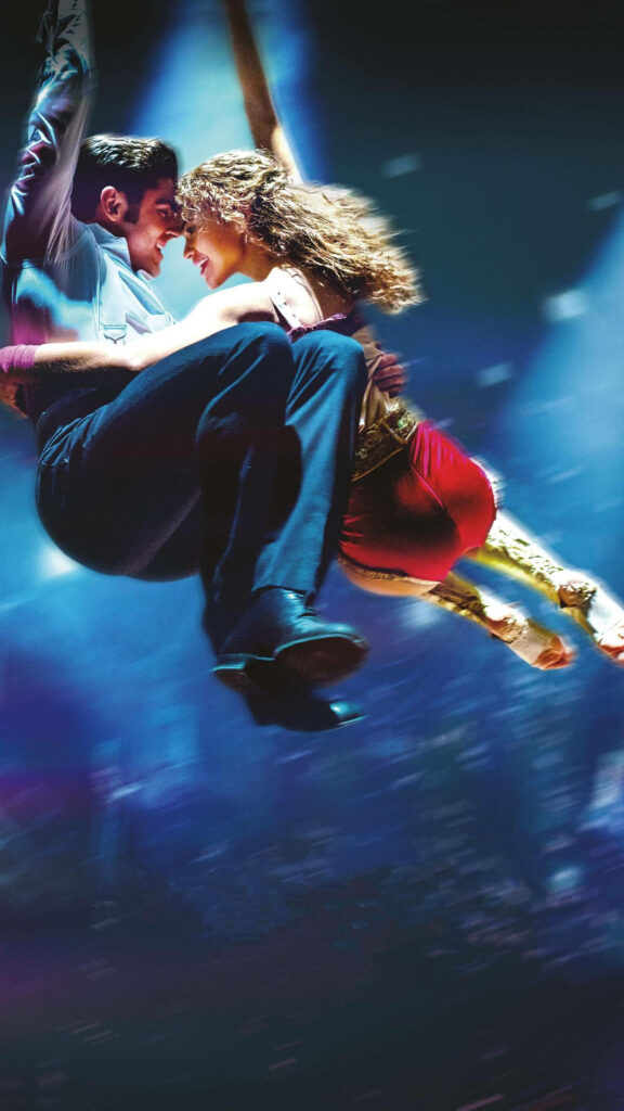 The Greatest Showman aerial performers soar under vibrant stage lights in a thrilling live act Wallpaper