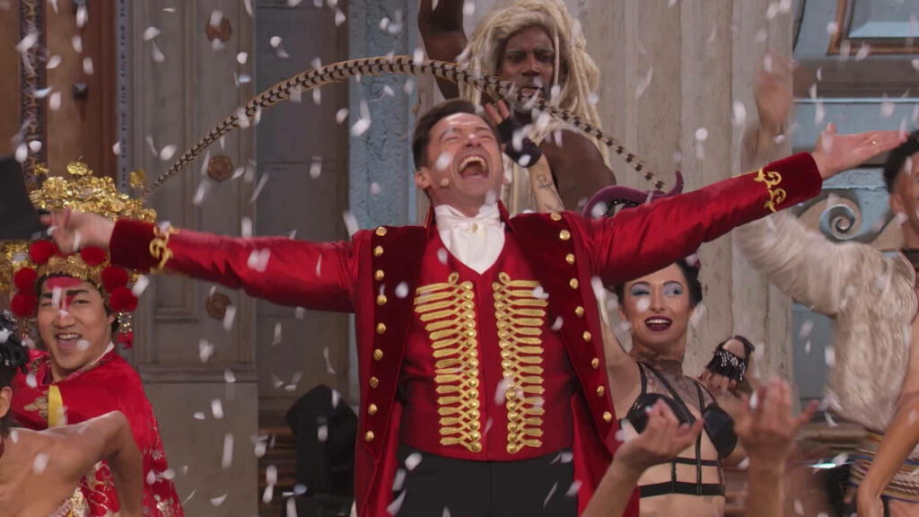 The Greatest Showman wallpaper vibrant ringmaster in red costume with performers and falling confetti
