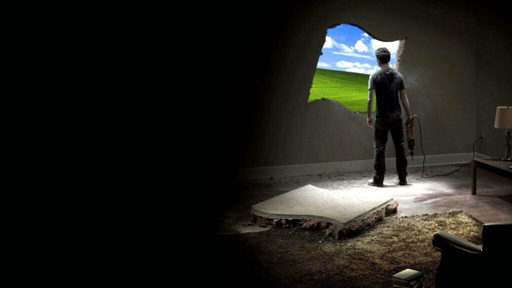 Man with power drill breaks wall revealing Windows XP Bliss landscape in dark concrete room Wallpaper