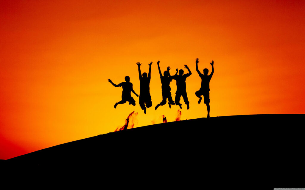 Sunset Soaring: Capturing the Joyful Silhouettes of Friends on a Mountain Top Wallpaper