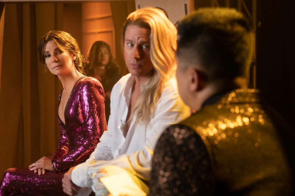 The Lost City movie wallpaper showing glamorous book launch scene with characters exchanging glances