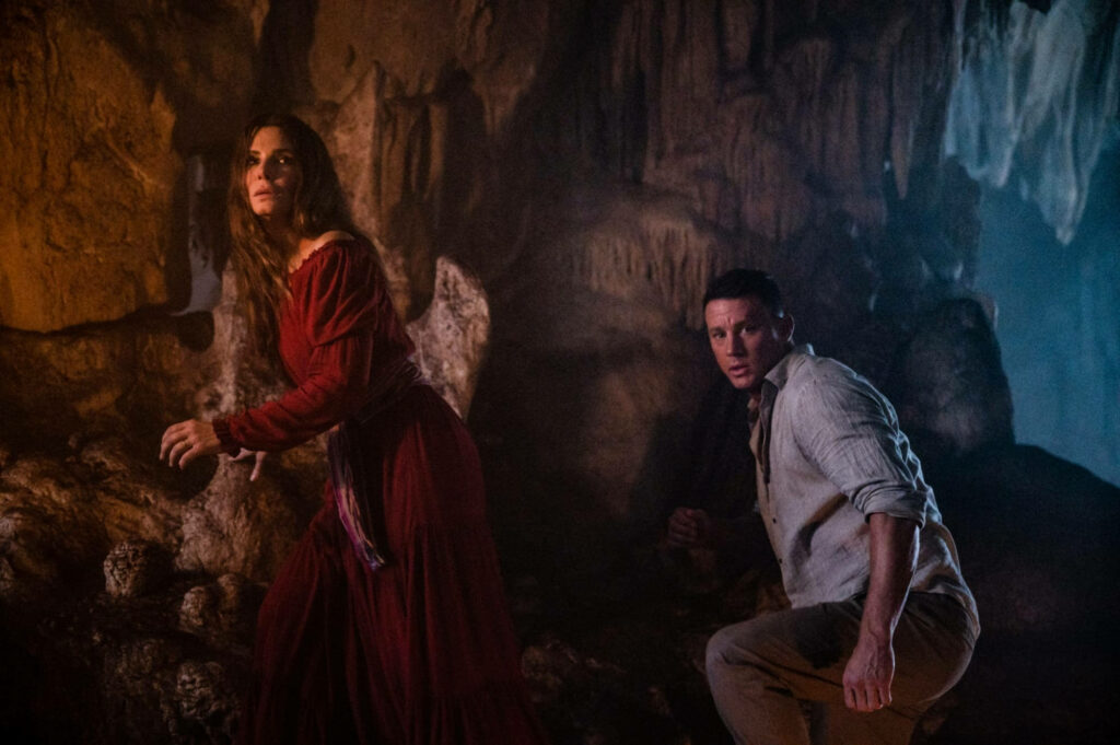 Two characters exploring a mysterious cave with rugged stone walls in The Lost City movie scene Wallpaper