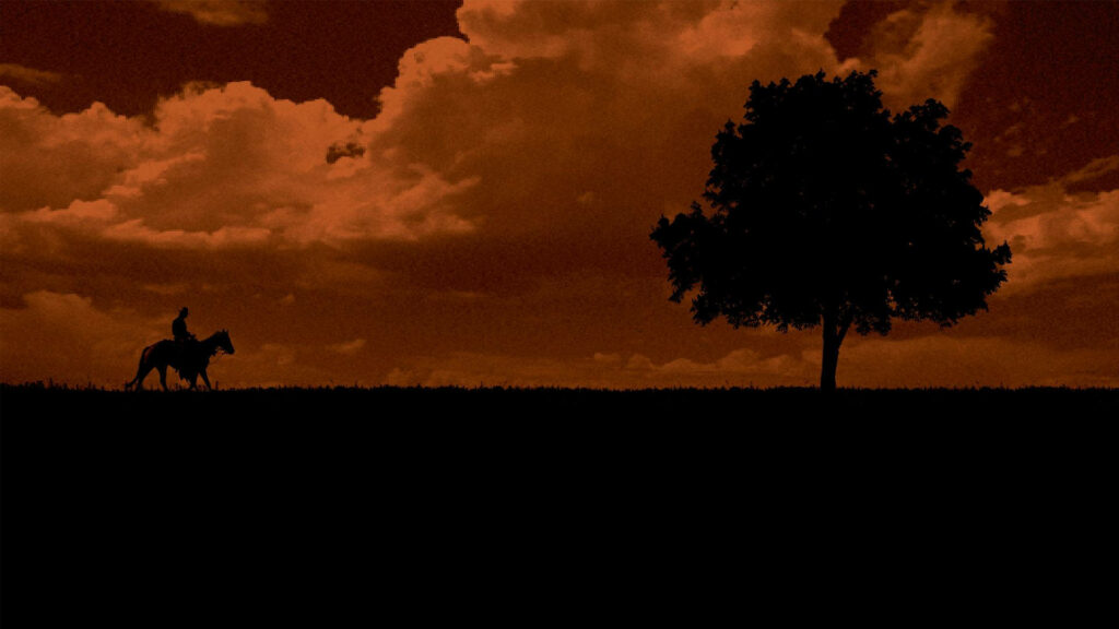 The Lone Rider: Majestic Western Cowboy Journeying under a Fiery Sunset Wallpaper