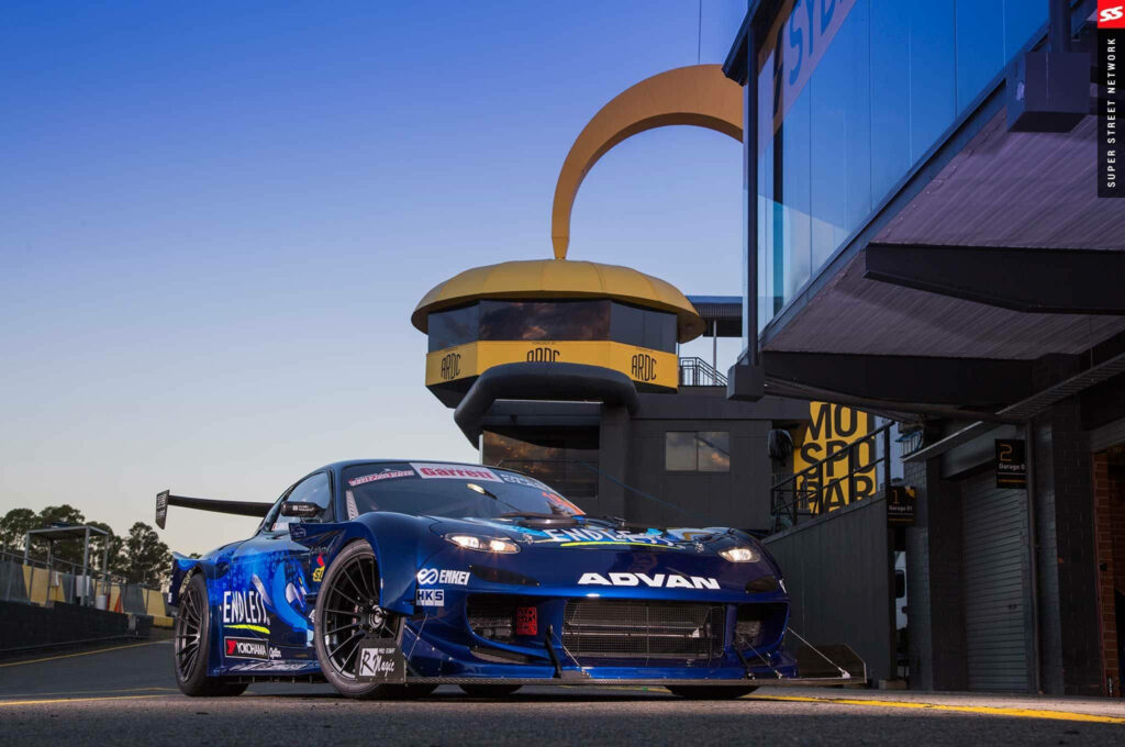 Captivating RX7 in the City: A Striking Blue Mazda RX-7 Showcased against a Striking Urban Landscape Wallpaper