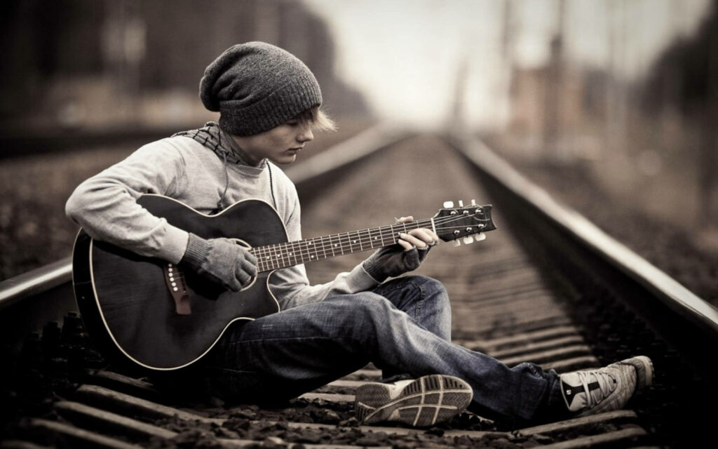 Solitude Strikes a Chord: A Captivating Image of a Teenage Guitarist Immersed in Railway Serenity Wallpaper