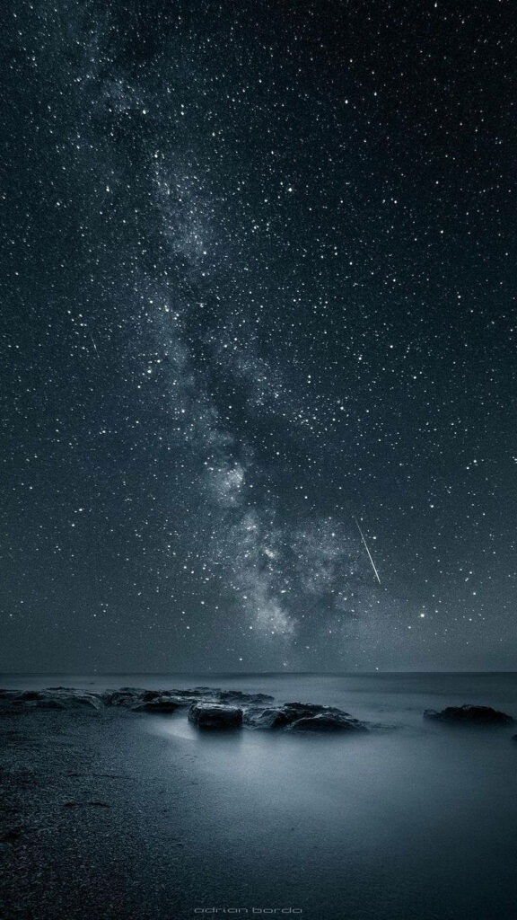Shoreline Stardust: A stunning night sky mobile wallpaper with glowing stars and passing meteor