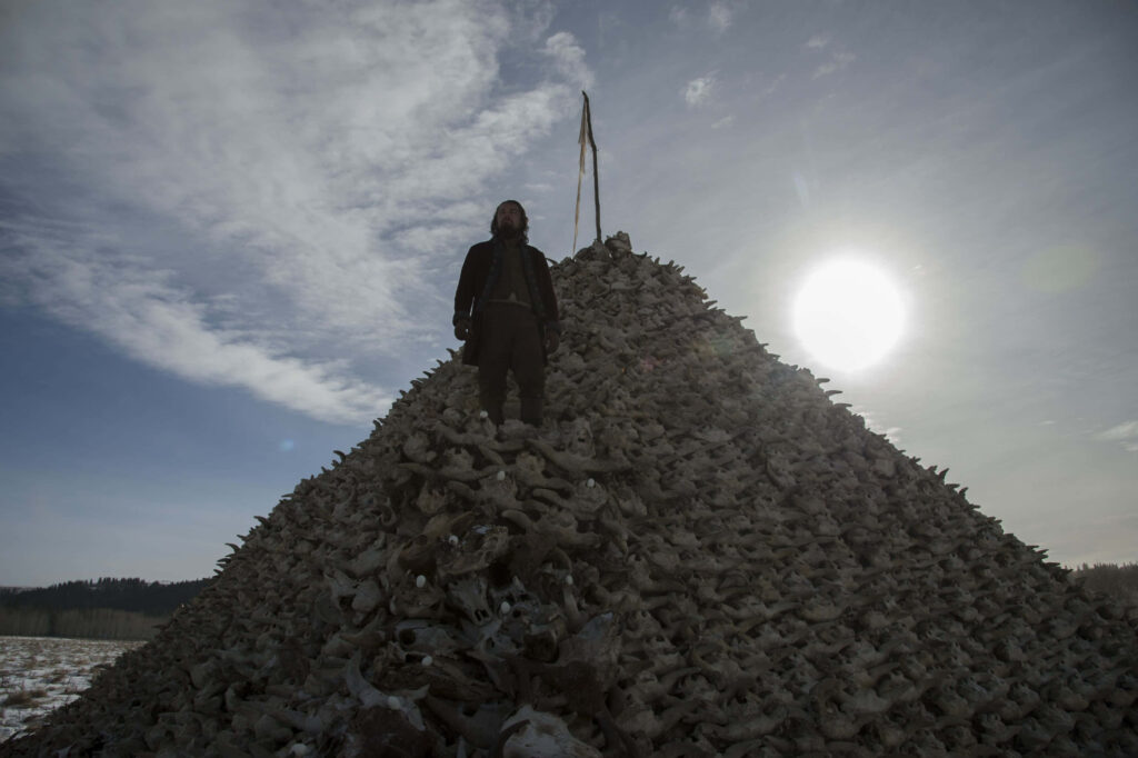 Dramatic Revenant wallpaper lone figure on skull pile under bright sun intense haunting scene