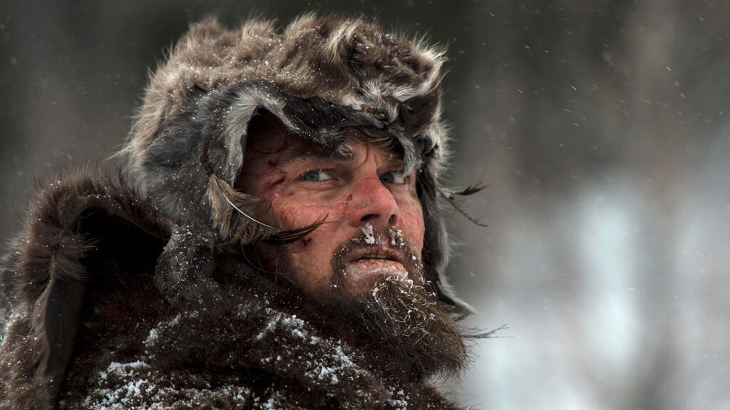 Rugged man in fur clothing stands determined in snowy wilderness scene from The Revenant film wallpaper
