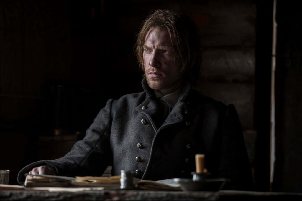 Somber Revenant wallpaper showing rugged character seated in dim cabin amid harsh wilderness
