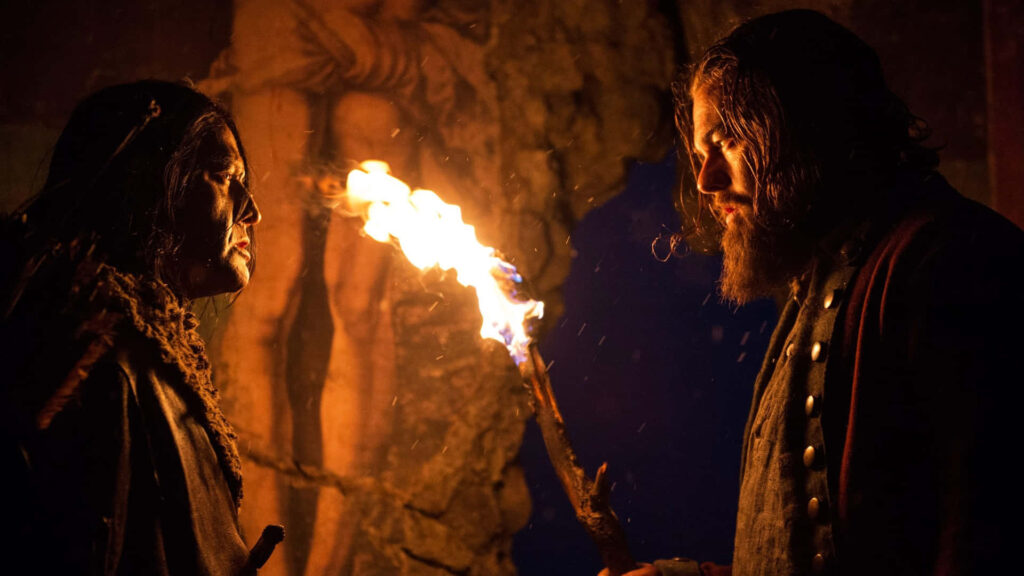 The Revenant wallpaper showing two men facing off by torchlight in a harsh wilderness setting