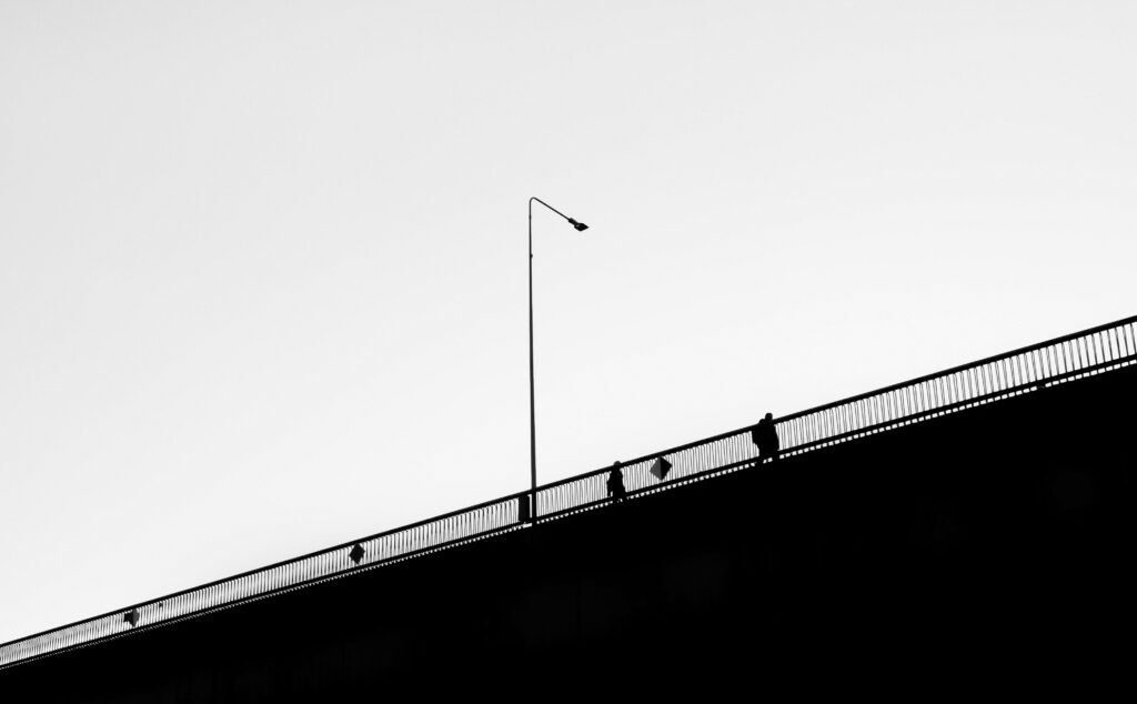 Monochrome Serenity: Individuals Gracefully Aligned on an Expansive Bridge Wallpaper