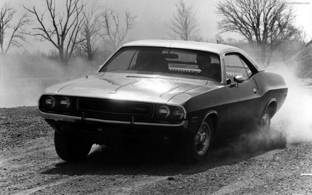 Black and White Vintage Snapshot: Dodge Challenger Speeds Across Gritty Terrain Wallpaper