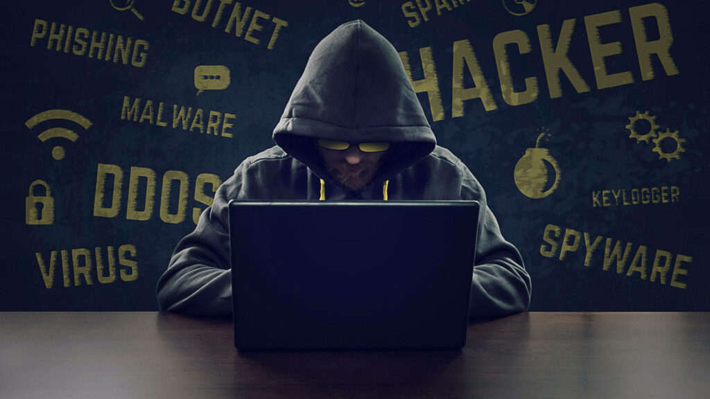 Cyber Cool: A Landscape of Hacking Words and a Hooded Hacker's Stylish Set-Up Wallpaper