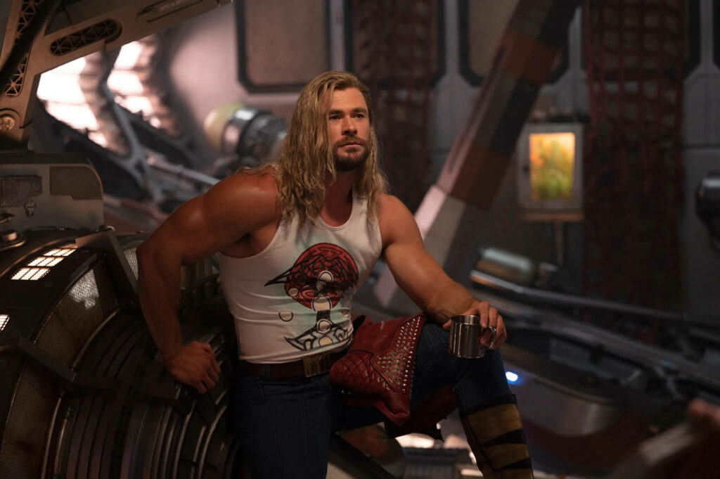 Thor muscular in graphic tank top holding metal cup sitting confidently in spaceship wallpaper