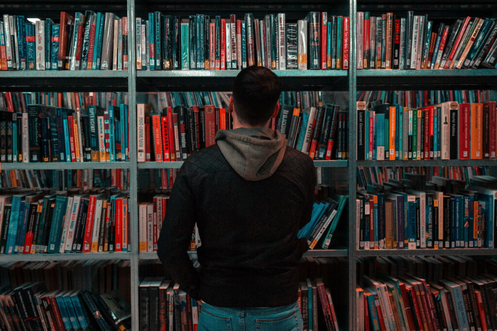 Thoughtful man stands by colorful bookshelves in library surrounded by knowledge and calm atmosphere Wallpaper