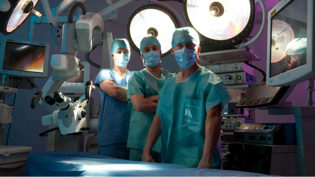 Three doctors in scrubs and masks stand in a high tech operating room with surgical lights Wallpaper