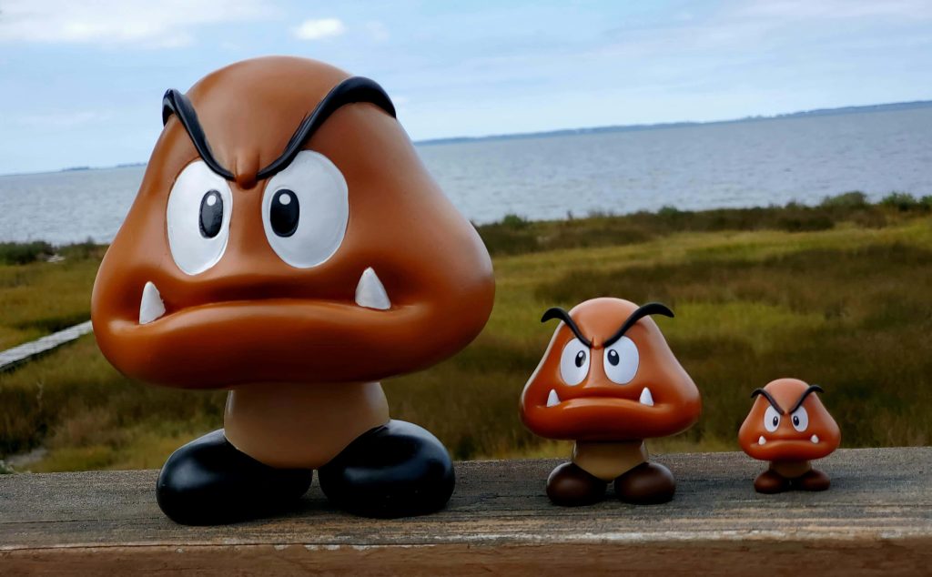 Three Super Mario Goomba figurines arranged by size on wooden railing outdoors wallpaper background