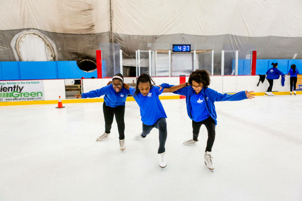 Three kids in matching blue outfits figure skating on bright ice rink for young skaters wallpaper