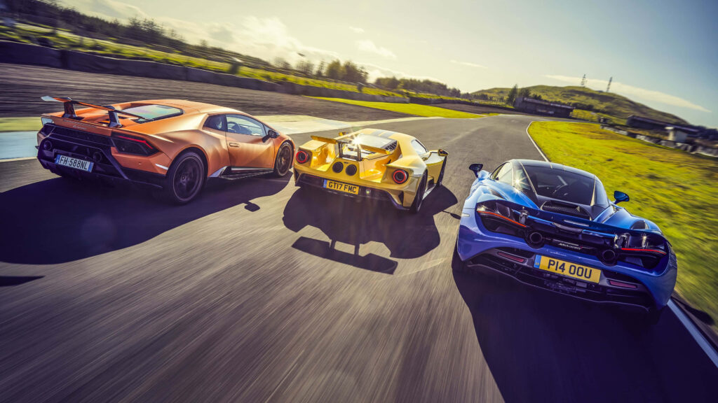 Three supercars racing side by side on sunlit track high speed intense motorsport competition wallpaper