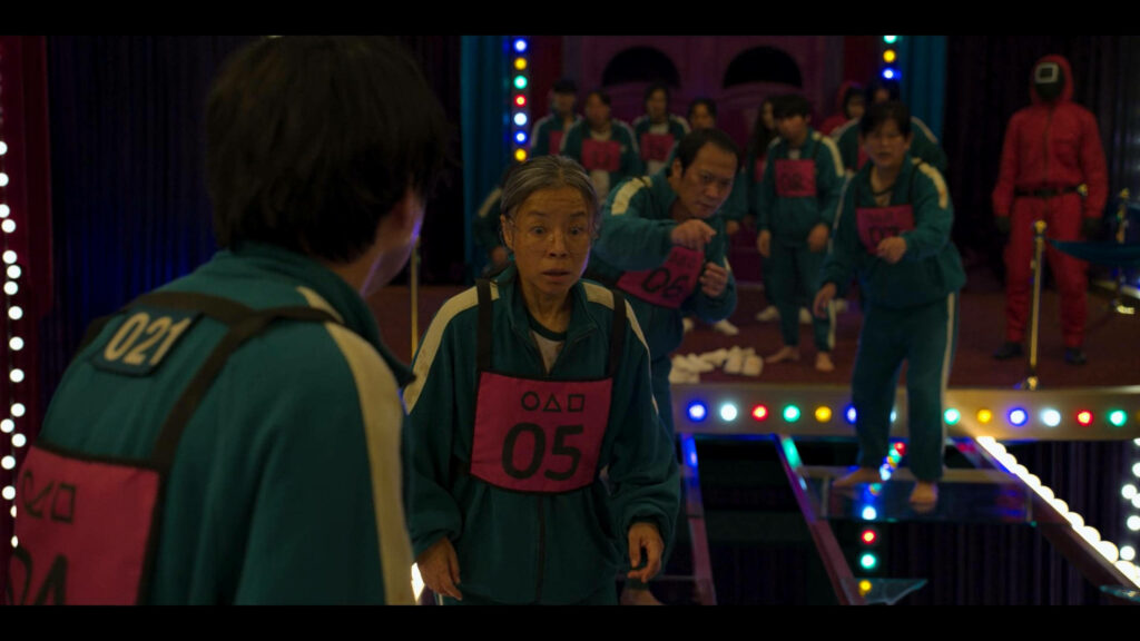 Thrilling Glass Bridge Challenge in Squid Game: Determined Participants Cross in Green Track Suits amidst Vibrant Lights Wallpaper