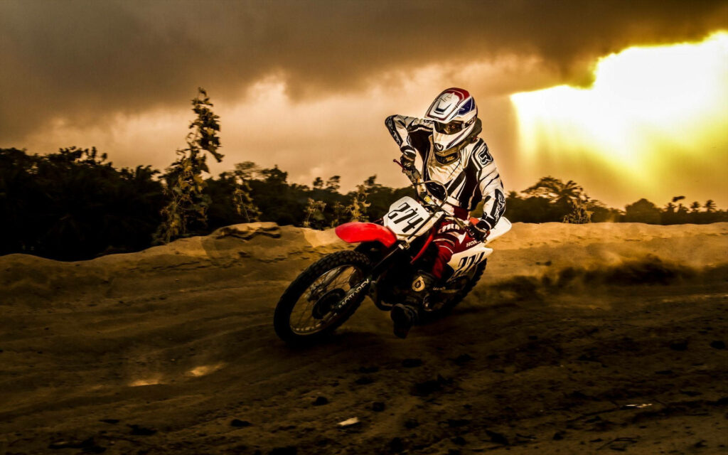 Thrilling Dirt Bike Rider Wallpaper: Rugged Field & Golden Sky