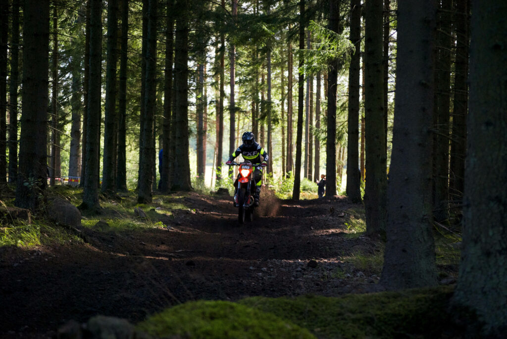 Dynamic Dirt Bike Rider in Dense Forest Trail - Adventure Wallpaper