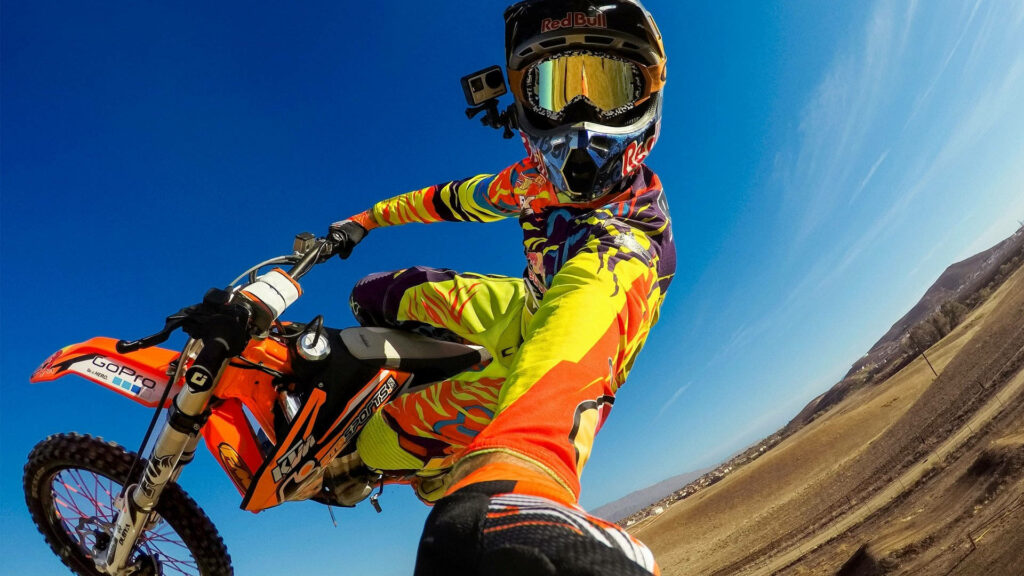 Thrilling motocross dirt bike rider mid-air in vibrant gear against clear blue sky wallpaper