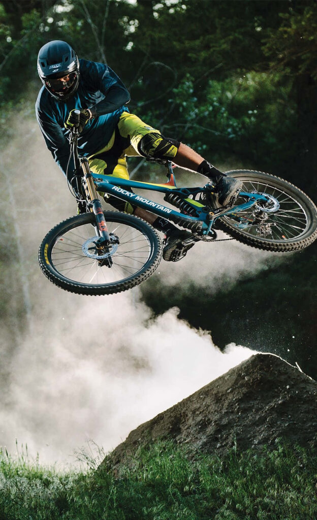 Thrilling Mountain Biking Wallpaper: Rider Mid-Air with Lush Greenery