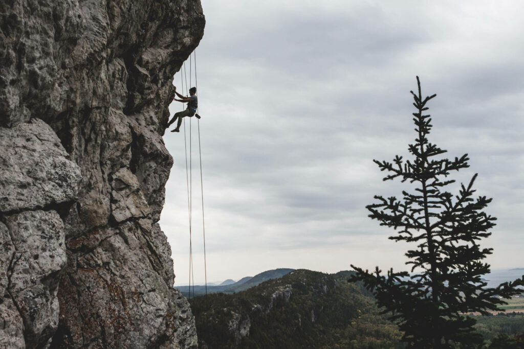 Man climbing rugged rock face with ropes under dramatic cloudy sky and distant mountains background Wallpaper