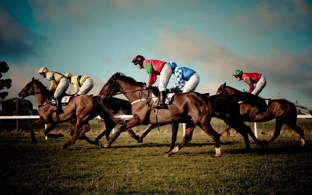 Jockeys racing thoroughbreds at full speed on grass track bright sky vibrant horse racing wallpaper