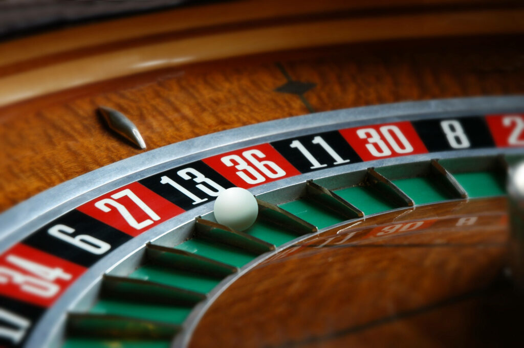 Close-up of spinning wooden roulette wheel with white ball on red black and green numbered slots Wallpaper